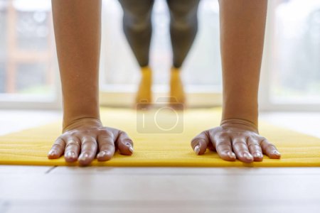 Hands pressed flat on yellow yoga mat, workout session indoors.