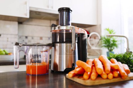 Juicer with fresh carrot juice on kitchen counter