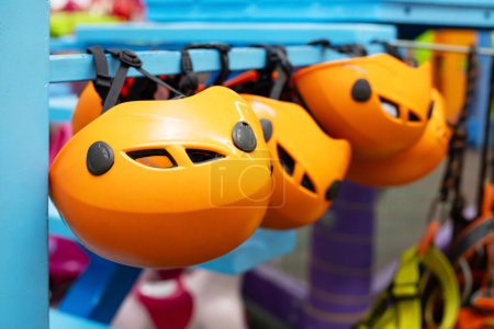 A series of orange safety climbing helmets with black straps hanging on a rack in a sports store.