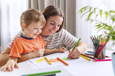 Foto de Una madre cariñosa apoyando a su hijo risueño mientras dibujan juntos, rodeados por una colorida variedad de lápices. - Imagen libre de derechos