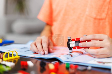 Close-up of childs hands assembling pieces of a red toy construction set, focusing with creativity and concentration.