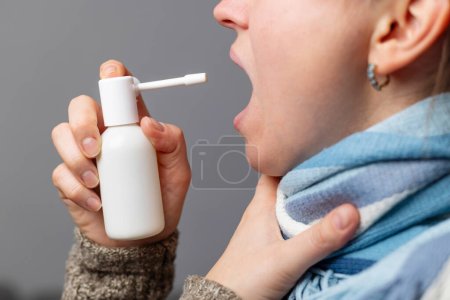 Acercamiento de una persona que se autoadministra aerosol de garganta, buscando alivio de los síntomas del dolor de garganta.