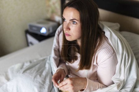 Intently watching a movie at home, a woman is engrossed in the projected imagery, experiencing cinematic entertainment.
