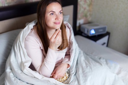 Woman wrapped in a blanket enjoying popcorn and a movie in bed