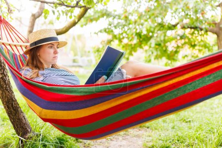 A relaxed woman reads a book in a vibrant hammock, shaded by greenery.