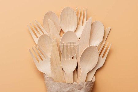 Foto de Cucharas y tenedores de madera biodegradables en una bolsa de papel sobre un fondo beige. - Imagen libre de derechos