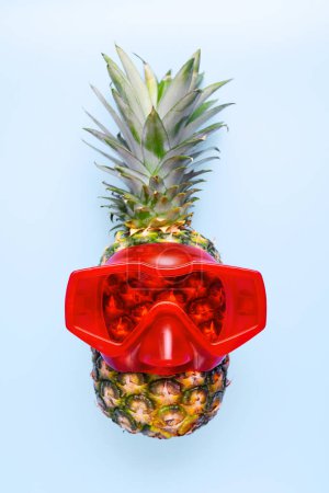 A quirky pineapple wearing red diving goggles against a stark blue background, tropical and humorous concept.