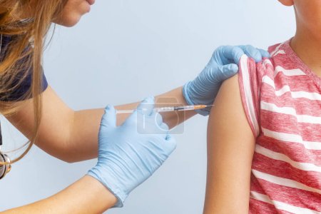 Un profesional sanitario que administra una vacuna a un brazo infantil con una jeringa, ambos con ropa casual.