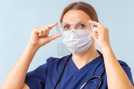 Healthcare worker with face mask fitting safety goggles in a clinical setting.