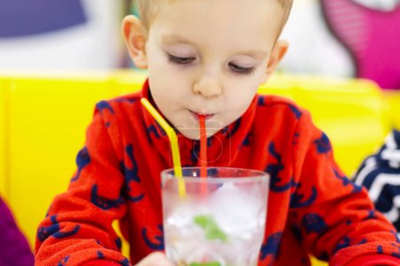 Kleiner Junge schlürft Wasser mit Minzblättern durch einen Strohhalm aus einem klaren Glas. Gesundes Getränk und Ernährungskonzept Design für Banner, Einladungen oder Lehrmaterialien mit Kopierraum.
