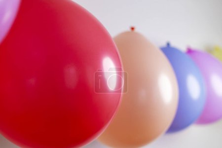 Multicolored balloons in a row with selective focus on a red balloon. Celebratory decorations concept. Design for greeting card, invitation, poster. Shallow depth of field with copy space.