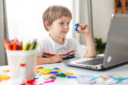 Young boy using laptop with educational toys. Home schooling setup. Early learning and technology integration concept. Design for banner, educational blog, and parenting guide.