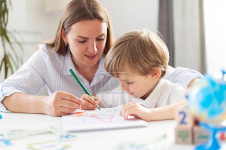 Woman and young boy drawing together at table. Casual home education scene. Early childhood development and parenting concept. Design for poster, banner, and educational materials.