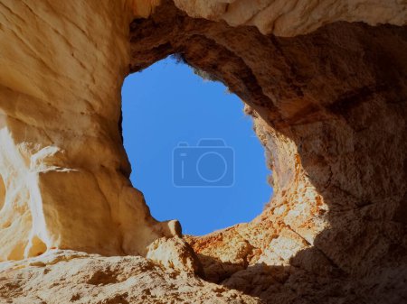 A hole in a cliff opens a view to the blue sky in Algarve Portugal