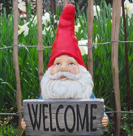 Enano de jardín con un sombrero rojo puntiagudo sosteniendo un cartel de bienvenida