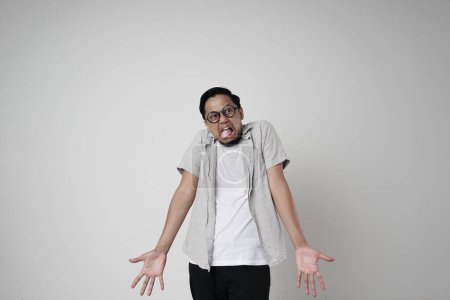 Foto de Un hombre asiático con una expresión despectiva saca su lengua mientras levanta sus manos agresivamente - Imagen libre de derechos