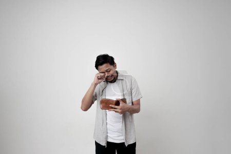 Foto de Estoy quebrado. Un hombre asiático triste y llorón que está quebrado mira su cartera vacía. El concepto de pobreza - Imagen libre de derechos