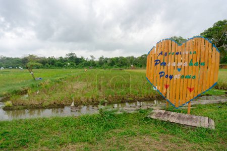 a welcome board labeled poyotomo rice field agritourism in a rice field area in the harvest season.