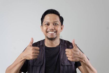 a man wearing a vest gives a good rating sign with a thumb gesture, good service. on a gray background