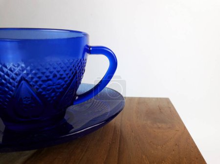 Una taza azul sobre una mesa de madera de teca y fondo blanco
