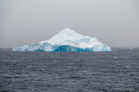 Téléchargez les photos : Un iceberg bleu abattu par une journée nuageuse en Antarctique - en image libre de droit