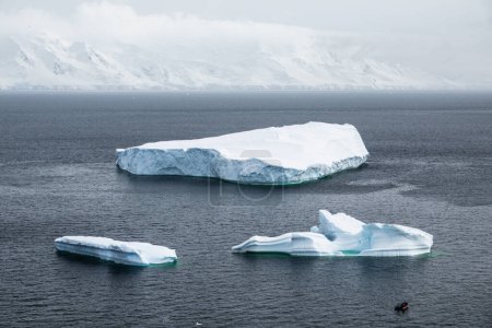 Photo for Palaver Point, Antarctic Peninsula - December 14, 2023 - Quark Expeditions zodiac boat stays in front of the group of large icebergs - Royalty Free Image