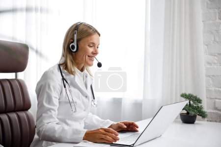 Telemedicina. Retrato en la cabeza de una doctora sonriente con auriculares mirando la cámara. Una médica mujer consulta remotamente en una reunión virtual en línea con un paciente. Medicina en línea.