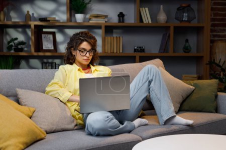 Seriöse junge Freiberuflerinnen, die freiberuflich von zu Hause aus arbeiten. Arbeitet auf dem Sofa am Laptop sitzend, fokussiertes Mädchen mit dem Computer, um zu Hause online zu lernen, weibliche Benutzerin, Internet-Fernarbeit, Programmierung.