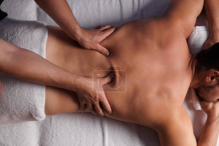 Photo for Handsome man having restorative back massage in spa salon, enjoying relaxing atmosphere, recharging after work. Masseuse gives therapeutic back massage to a visitor, the concept of healthy lifestyle - Royalty Free Image