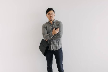 Foto de Asiático tailandés hombre de negocios utilizando el teléfono móvil aislado sobre la pared de fondo blanco y sosteniendo bolsa de carpeta de archivo negro mientras está de pie y mirando a la cámara. - Imagen libre de derechos