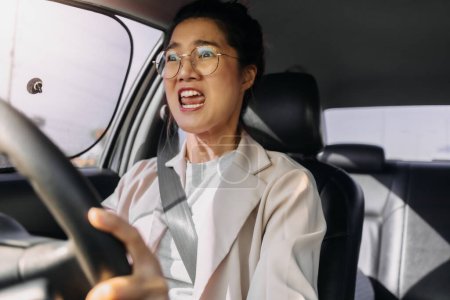 Téléchargez les photos : Asiatique femme thaïlandaise porter des lunettes de vue, à haute température tout en conduisant une voiture sur la route, se fâcha avec un mauvais trafic à l'heure de pointe le matin tout en allant au travail. - en image libre de droit