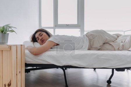 Téléchargez les photos : Asiatique femme thaïlandaise dormir face contre terre sur le ventre, couché sur un lit blanc, faisant un bon rêve, somnolent le matin dans la chambre d'appartement. - en image libre de droit