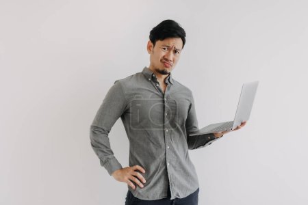 Photo for Asian man with beard wear grey shirt, dislike unsatisfied face, holding notebook hand gesture, unhappy face looking at camera isolated over white background wall. - Royalty Free Image