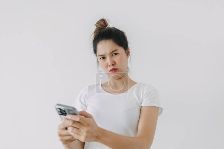Photo for Asian Thai woman using mobile phone with funny doubt face, holding smartphone by silent suspicious posing, standing isolated over white background wall. High quality photo - Royalty Free Image
