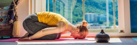 BANNER, LONG FORMAT Achtsame gesunde Frau, die zu Hause Yoga praktiziert. Auf dem Boden sitzen und Yoga machen, um das geistige Gleichgewicht zu stärken und Stress abzubauen. Die Zeit genießen nutzt einen Aromadiffusor.