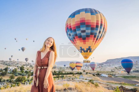 Foto de Mujer turista mirando globos aerostáticos en Capadocia, Turquía. Feliz viaje en Turquía concepto. Mujer en la cima de una montaña disfrutando de una vista maravillosa. - Imagen libre de derechos