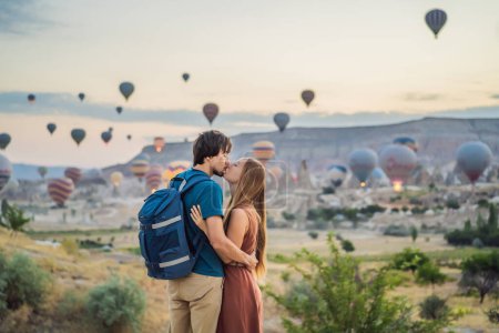 Foto de Turistas pareja hombre y mujer mirando globos de aire caliente en Capadocia, Turquía. Feliz viaje en Turquía concepto. Pareja hombre y mujer en una cima de la montaña disfrutando de una vista maravillosa. - Imagen libre de derechos