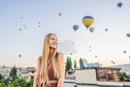 Foto de Mujer turista mirando globos aerostáticos en Capadocia, Turquía. Feliz viaje en Turquía concepto. Mujer en la cima de una montaña disfrutando de una vista maravillosa. - Imagen libre de derechos