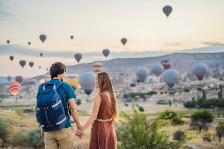 Foto de Turistas pareja hombre y mujer mirando globos de aire caliente en Capadocia, Turquía. Feliz viaje en Turquía concepto. Pareja hombre y mujer en una cima de la montaña disfrutando de una vista maravillosa. - Imagen libre de derechos