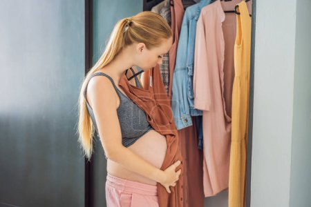 A pregnant woman has nothing to wear. A pregnant woman stands in front of a closet with clothes and does not know what to wear because the clothes do not fit on her.