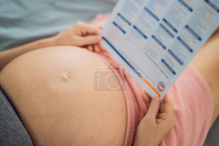 Foto de Una mujer embarazada observa los resultados de un análisis de sangre impreso en papel. - Imagen libre de derechos
