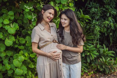 Téléchargez les photos : Un moment chaleureux capturé dans le parc en tant que femme enceinte après 40 ans partage un lien spécial avec sa fille adolescente, embrassant la beauté de la connexion mère-fille. - en image libre de droit