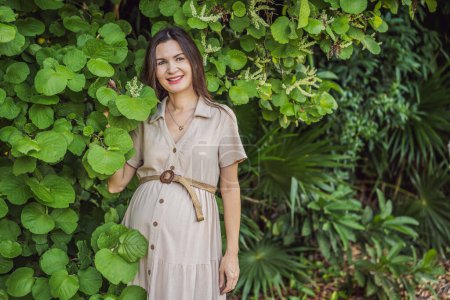 Téléchargez les photos : Une femme enceinte sereine et rayonnante après 40 ans, entourée par la beauté de la nature dans le parc, chérissant le voyage de la maternité avec un sourire rayonnant. - en image libre de droit