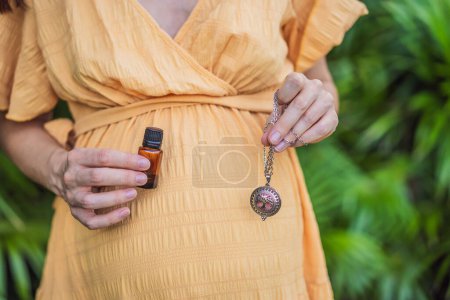 Téléchargez les photos : Femme enceinte après 40 démontrant l'utilisation d'un pendentif d'arôme, combinant style et aromathérapie pendant son voyage de grossesse. - en image libre de droit