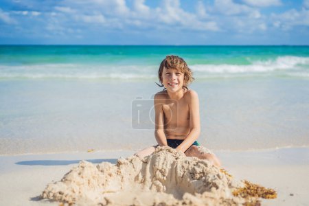 Téléchargez les photos : Jeunes garçons pur délice comme il explore le terrain de jeu sablonneux de la plage, façonnant des rêves avec des grains de sable. - en image libre de droit