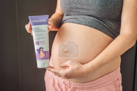 Photo for Mexico, Cancun, 02.02.2022: Mom to mom cream for stretch marks for pregnant women. Positive young pregnant woman in comfortable homewear applying belly butter on her big tummy, woman belly. - Royalty Free Image