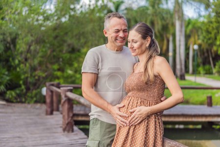 Téléchargez les photos : Un couple heureux et âgé de plus de 40 ans, profitant d'une promenade tranquille dans un parc, leur joie évidente alors qu'ils embrassent le voyage de la grossesse plus tard dans la vie. - en image libre de droit