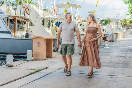 Téléchargez les photos : Un couple heureux et âgé de plus de 40 ans, profitant d'une promenade tranquille sur le front de mer, leur joie évidente alors qu'ils embrassent le voyage de la grossesse plus tard dans la vie. - en image libre de droit