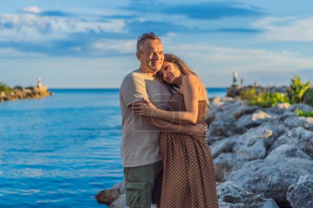 Foto de Una pareja feliz y madura de más de 40 años, disfrutando de un tranquilo paseo por el paseo marítimo On the Sunset, su alegría evidente al abrazar el viaje del embarazo más adelante en la vida. - Imagen libre de derechos