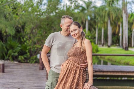 Téléchargez les photos : Un couple heureux et âgé de plus de 40 ans, profitant d'une promenade tranquille dans un parc, leur joie évidente alors qu'ils embrassent le voyage de la grossesse plus tard dans la vie. - en image libre de droit